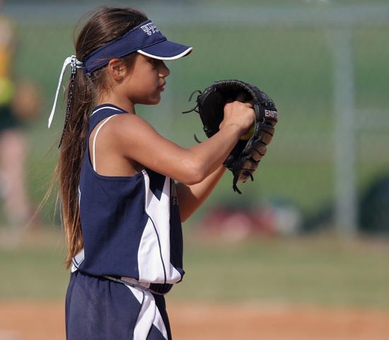 young girl in baseball uniform about to pitch